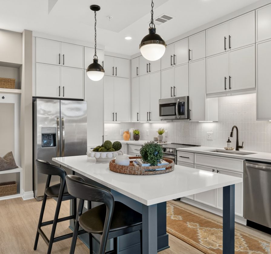 Modern kitchen with white cabinets, stainless steel appliances, and a central island with two black chairs.