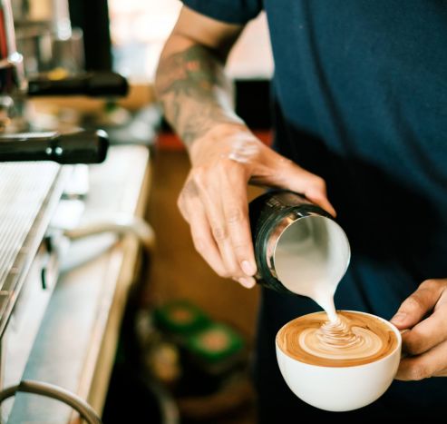 Barista pours steamed milk into a cup of coffee, creating latte art on the surface.