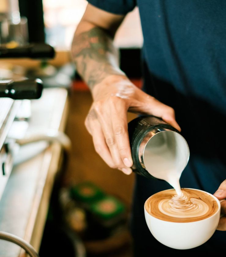 Barista pours steamed milk into a cup of coffee, creating latte art on the surface.
