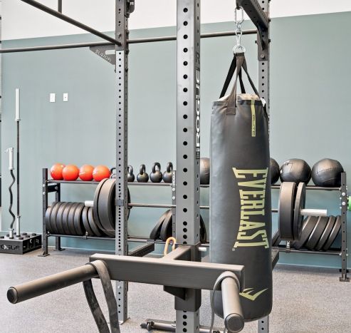 Modern gym with weight racks, benches, exercise bike, mirrored walls, and overhead lighting in a spacious, clean room.
