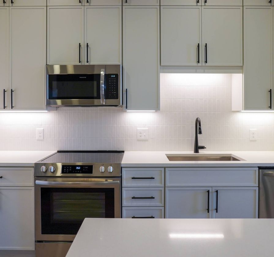 Modern kitchen with white cabinets, stainless steel appliances, sink, and under-cabinet lighting.